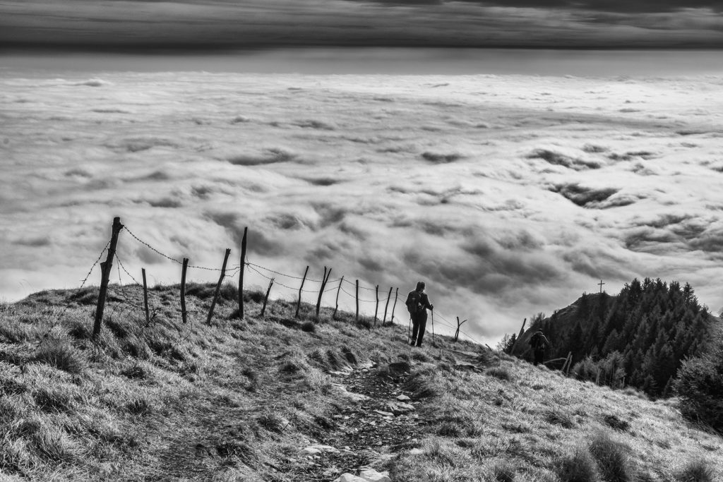 Persona che cammina in montagna, davanti solo un mare di nuvole, bianco e nero